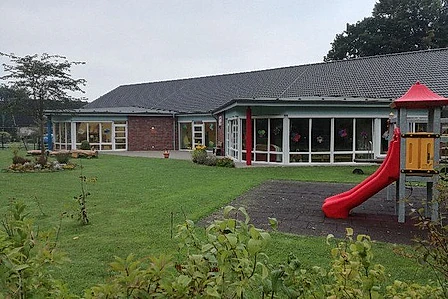 Kirchenkindergarten mit Spielplatz an bewölktem Tag.