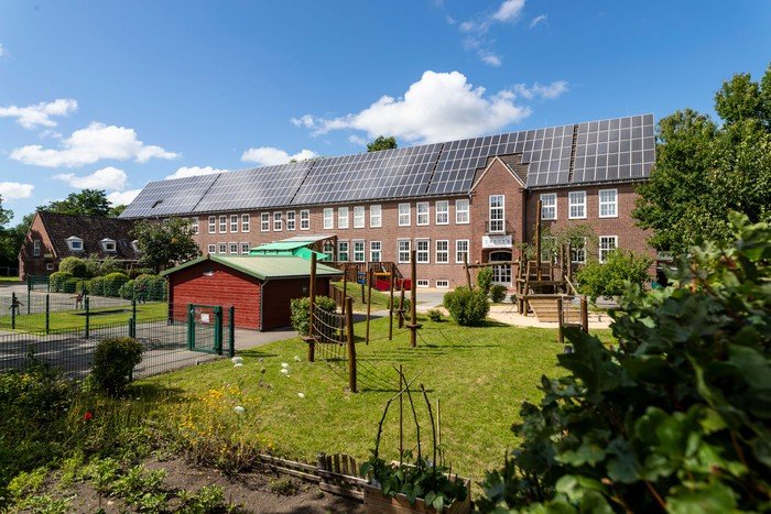 Kindergarten mit Solaranlage und Spielgeräten im Freien.